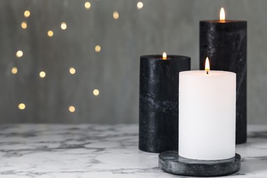 Burning candles on white marble table against blurred lights, space for text