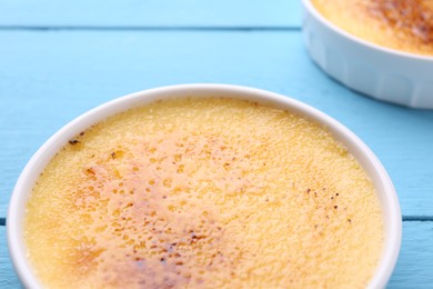 Photo of Delicious creme brulee in bowl on light blue wooden table, closeup