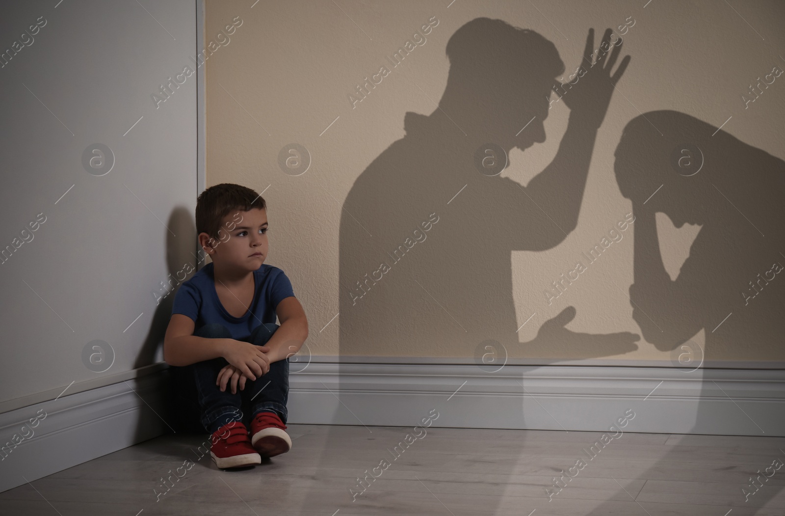 Image of Little boy sitting in corner near yellow wall and silhouettes of arguing parents 