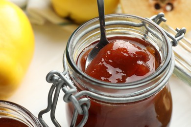 Photo of Taking tasty homemade quince jam from jar on blurred background, closeup