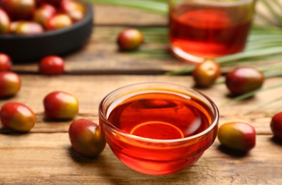 Photo of Palm oil in glass bowl, tropical leaf and fruits on wooden table