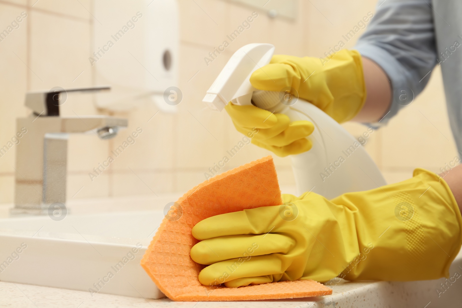 Photo of Woman cleaning sink with detergent and rag in bathroom, closeup