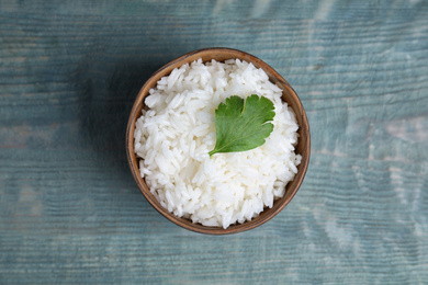 Photo of Bowl with tasty cooked rice on light blue wooden table, top view