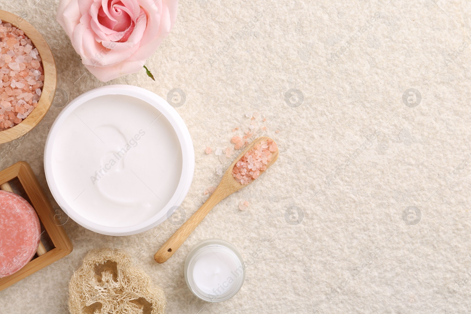 Photo of Flat lay composition with moisturizing cream in open jar and other body care products on light textured table. Space for text