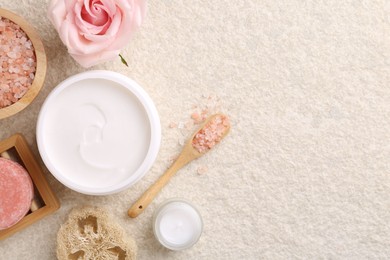 Photo of Flat lay composition with moisturizing cream in open jar and other body care products on light textured table. Space for text