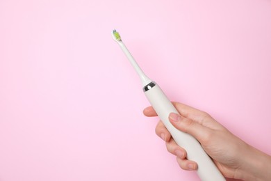 Woman holding electric toothbrush on pink background, closeup