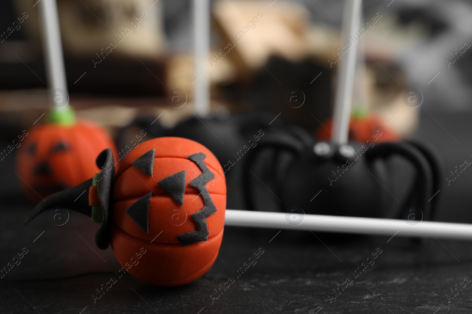 Photo of Pumpkin shaped cake pop on black table, closeup. Halloween treat