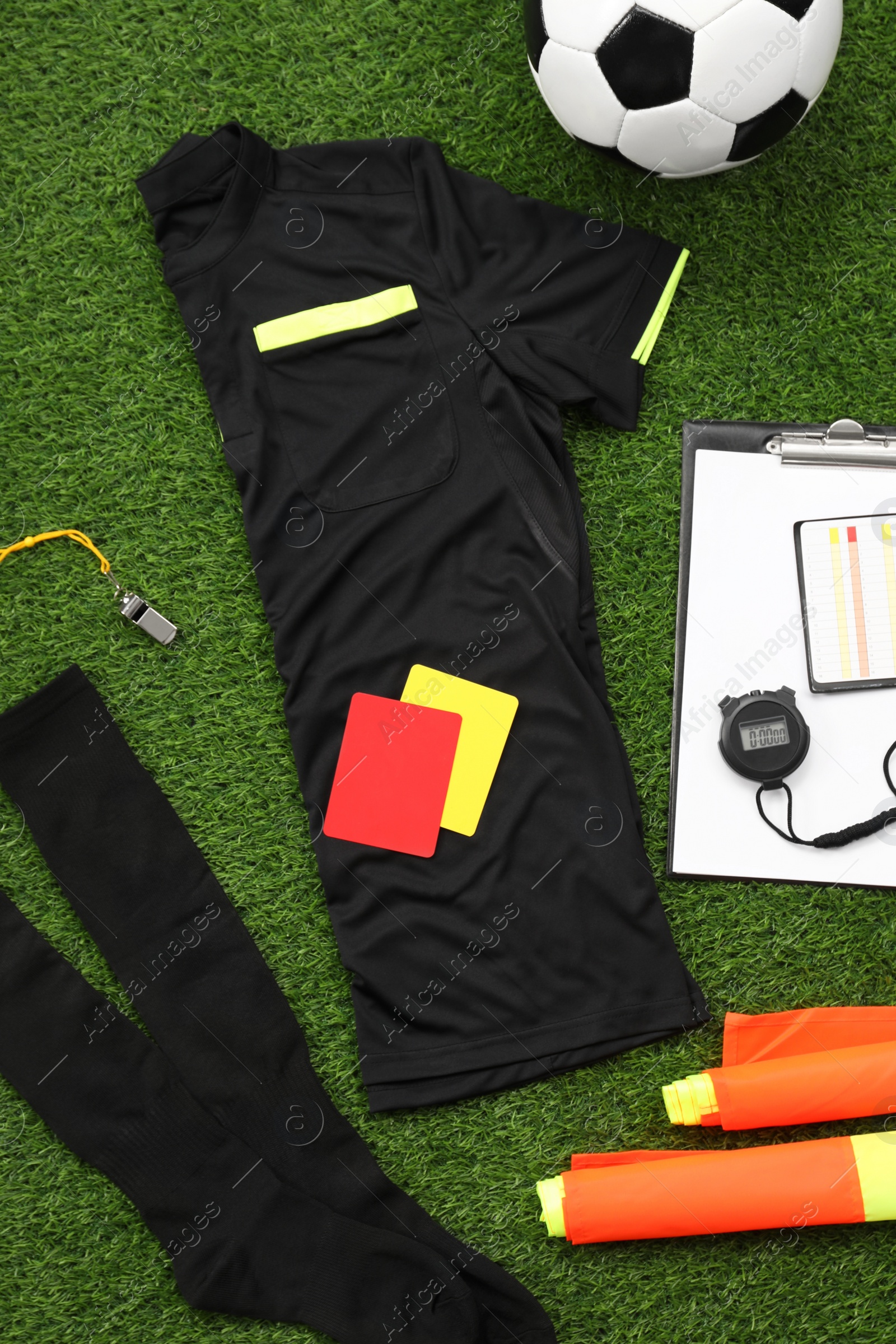 Photo of Uniform, soccer ball and other referee equipment on green grass, flat lay