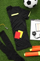 Uniform, soccer ball and other referee equipment on green grass, flat lay