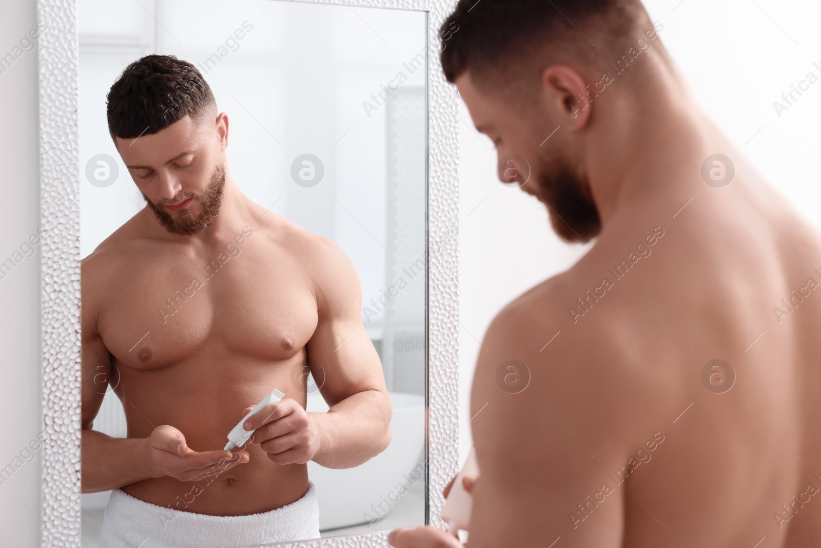 Photo of Handsome man applying body cream near mirror in bathroom