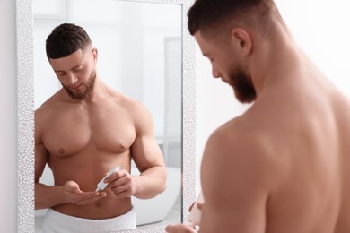 Handsome man applying body cream near mirror in bathroom