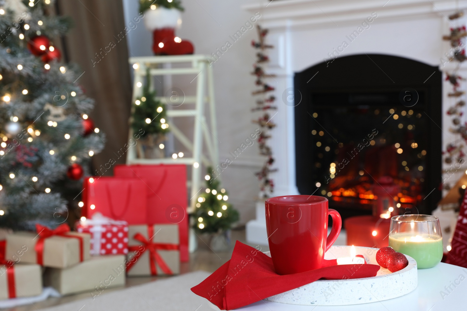 Photo of Candles and red cup on white table in room with Christmas decorations. Festive interior design