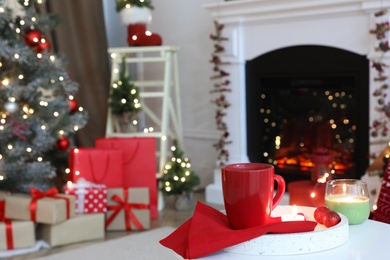 Candles and red cup on white table in room with Christmas decorations. Festive interior design