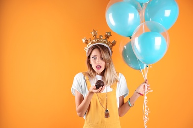 Young woman with birthday muffin and air balloons on color background