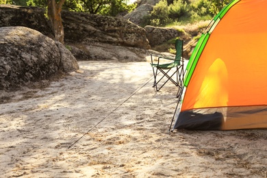 Photo of Modern camping tent and chair in wilderness. Space for text