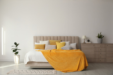 Photo of Stylish bedroom interior with soft yellow pillows and blanket