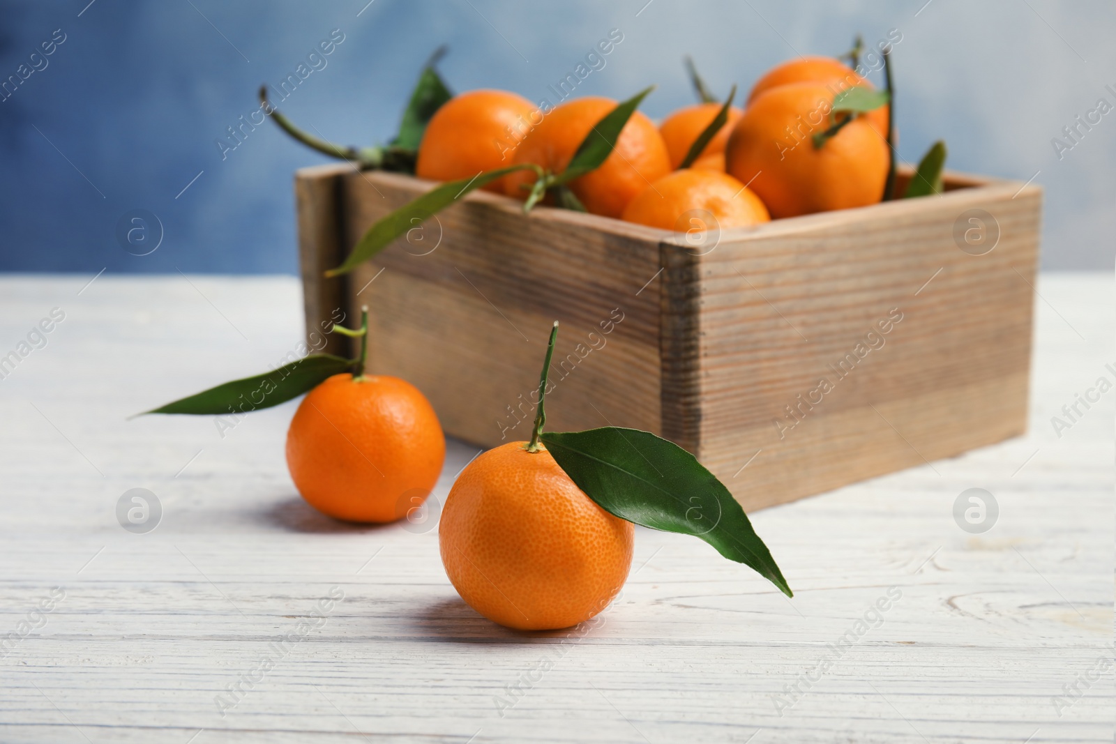 Photo of Fresh ripe tangerines with green leaves and wooden crate on table