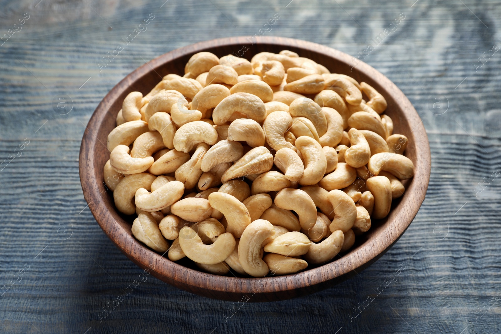 Photo of Tasty cashew nuts in bowl on wooden table