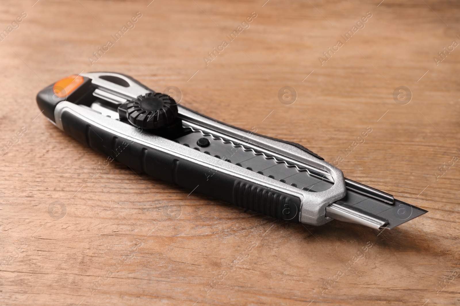 Photo of Utility knife on wooden table, closeup. Construction tool