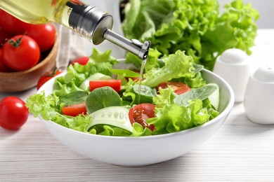 Photo of Pouring oil into delicious vegetable salad on white wooden table, closeup