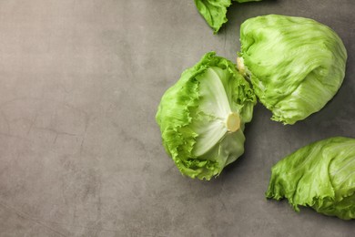 Fresh green iceberg lettuce heads and leaves on grey table, flat lay. Space for text