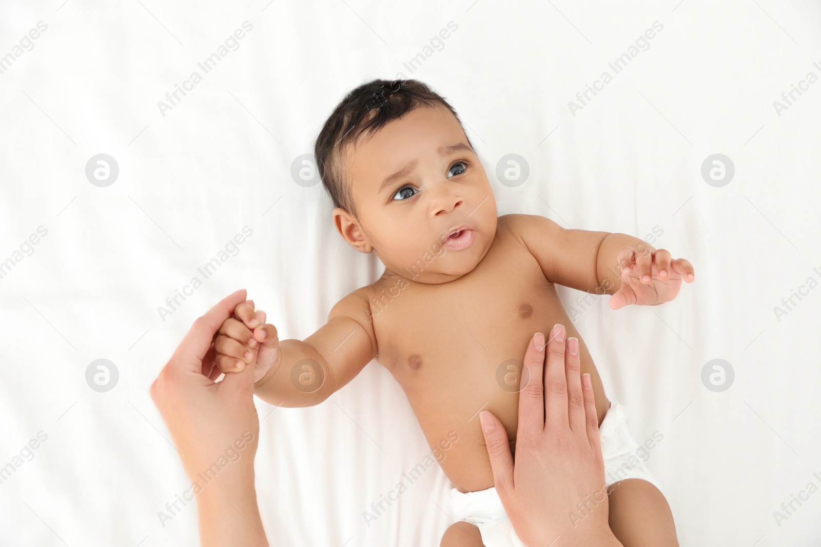 Photo of Mother and her cute child on white bed, top view. Baby massage and exercises