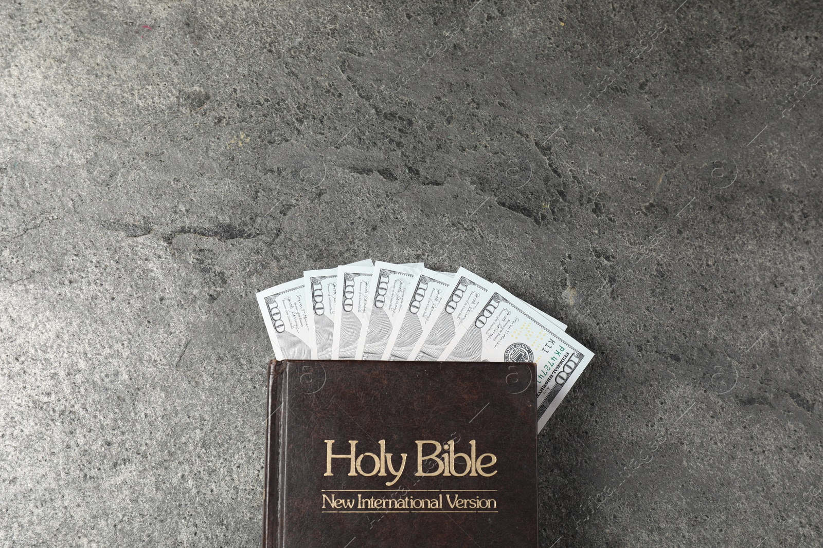 Photo of Holy Bible and money on grey table, top view. Space for text