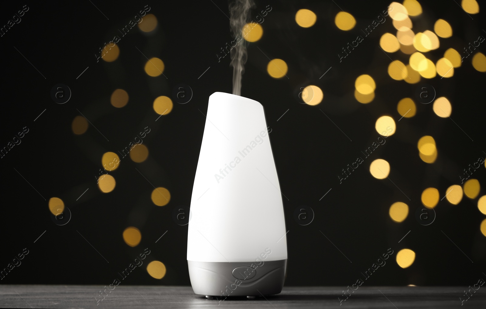 Photo of Modern aroma humidifier on wooden table against blurred lights, space for text