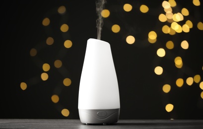 Modern aroma humidifier on wooden table against blurred lights, space for text