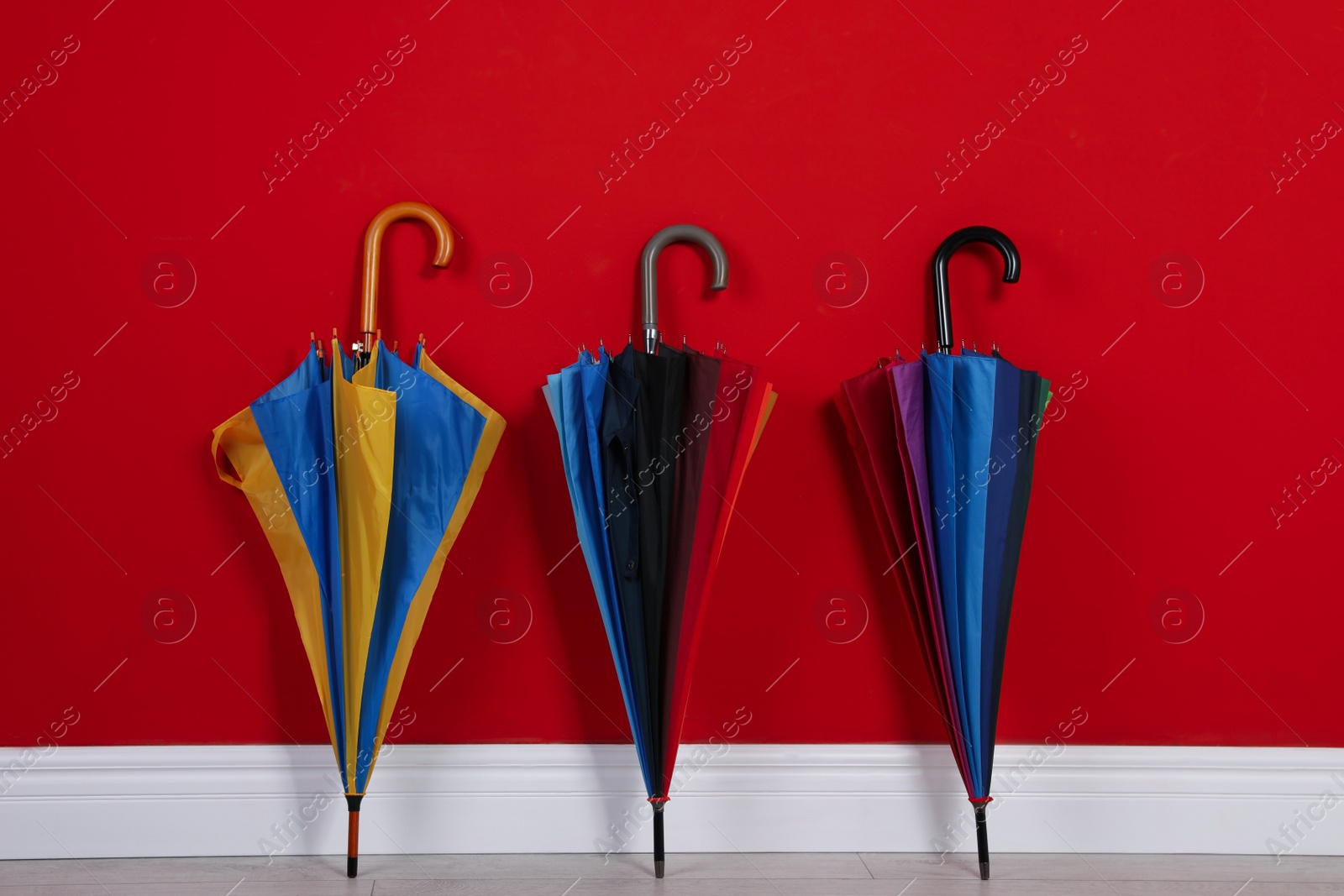 Photo of Beautiful closed colorful umbrellas near red wall