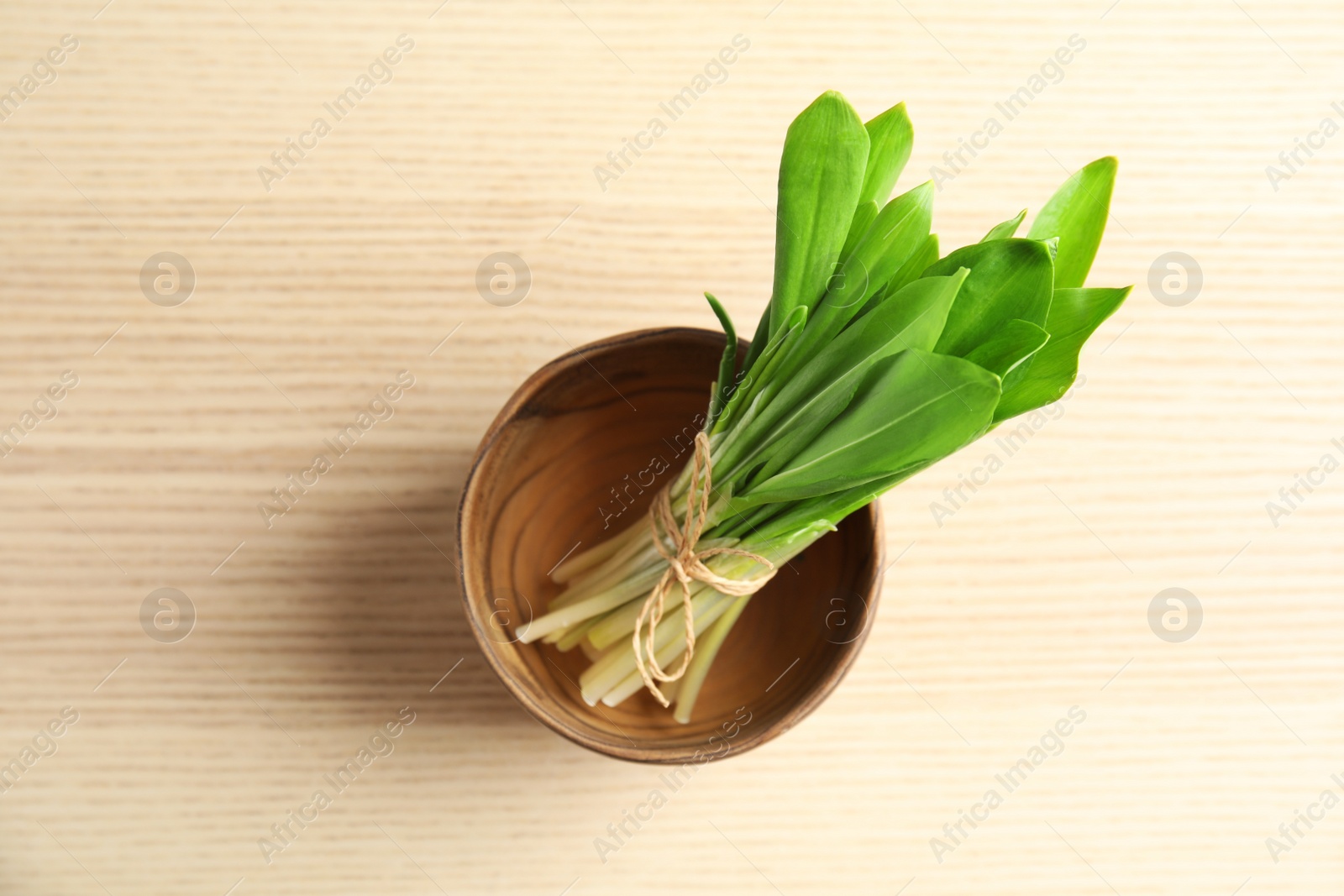 Photo of Bowl with bunch of wild garlic or ramson on wooden table, top view
