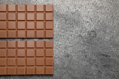 Photo of Delicious milk chocolate bars on grey table, flat lay. Space for text