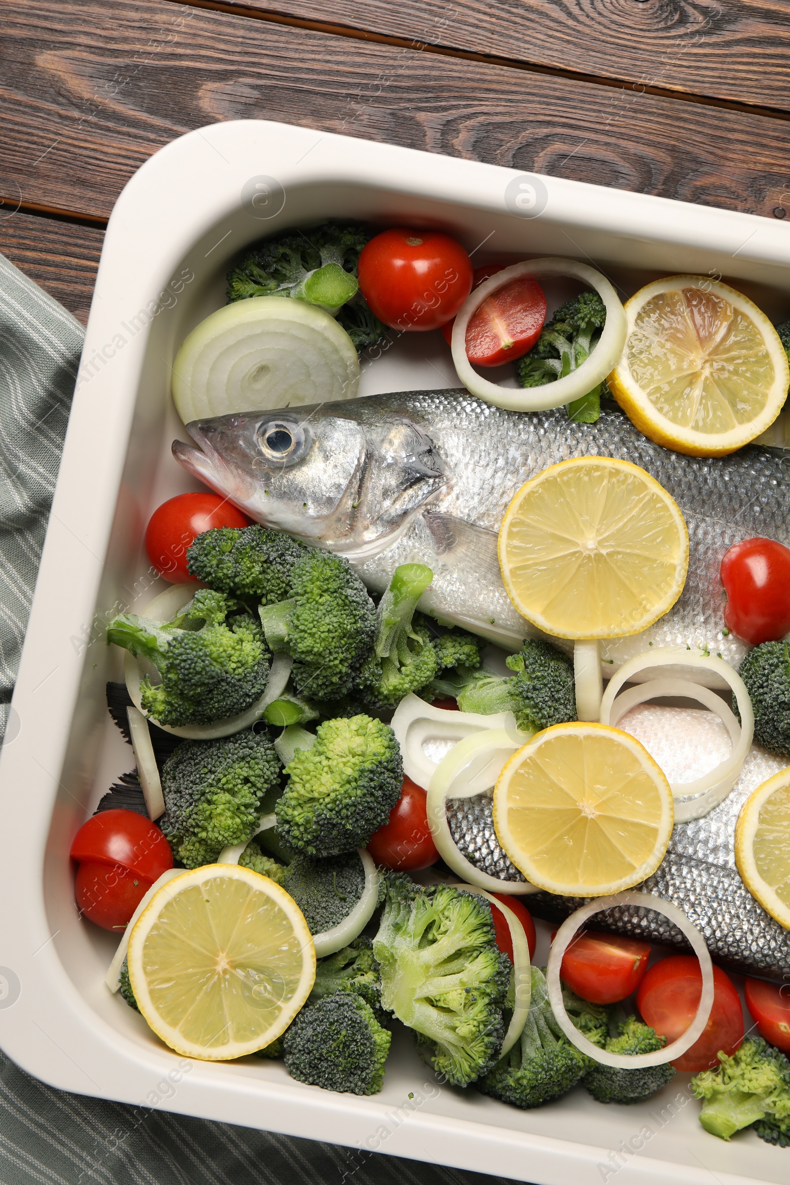 Photo of Raw fish with vegetables and lemon in baking dish on wooden table, top view