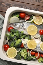 Raw fish with vegetables and lemon in baking dish on wooden table, top view