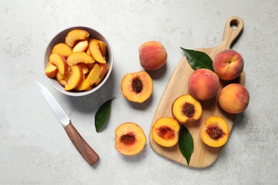 Delicious juicy peaches, leaves and knife on light grey textured table, flat lay