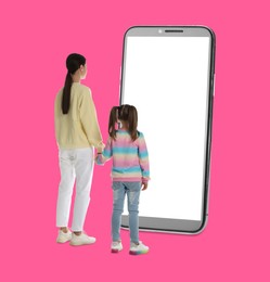 Mother with her daughter standing in front of big smartphone on pink background