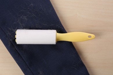 Photo of Lint roller and sleeve of jacket covered with hair on wooden table, flat lay