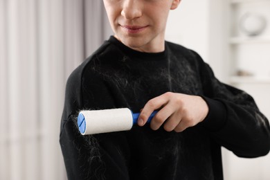 Pet shedding. Man with lint roller removing dog's hair from sweater at home, closeup