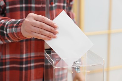 Photo of Woman putting her vote into ballot box on blurred background, closeup