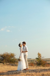 Happy newlyweds with beautiful field bouquet outdoors