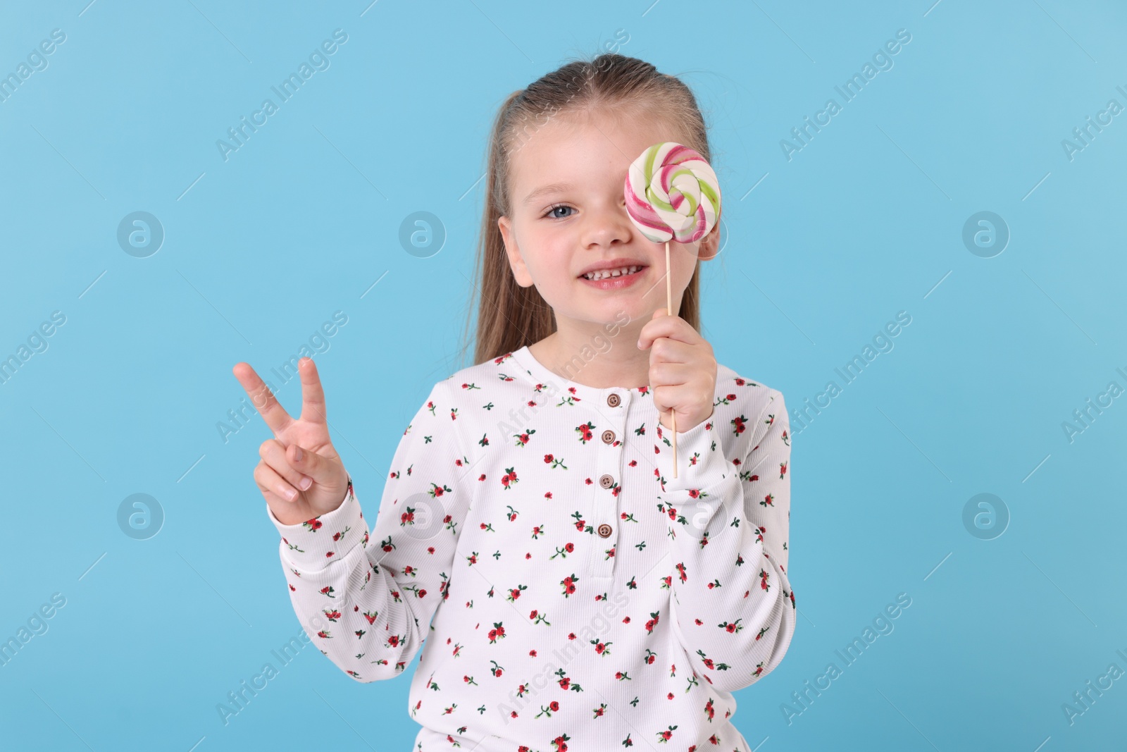 Photo of Happy little girl with colorful lollipop swirl on light blue background