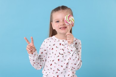 Happy little girl with colorful lollipop swirl on light blue background