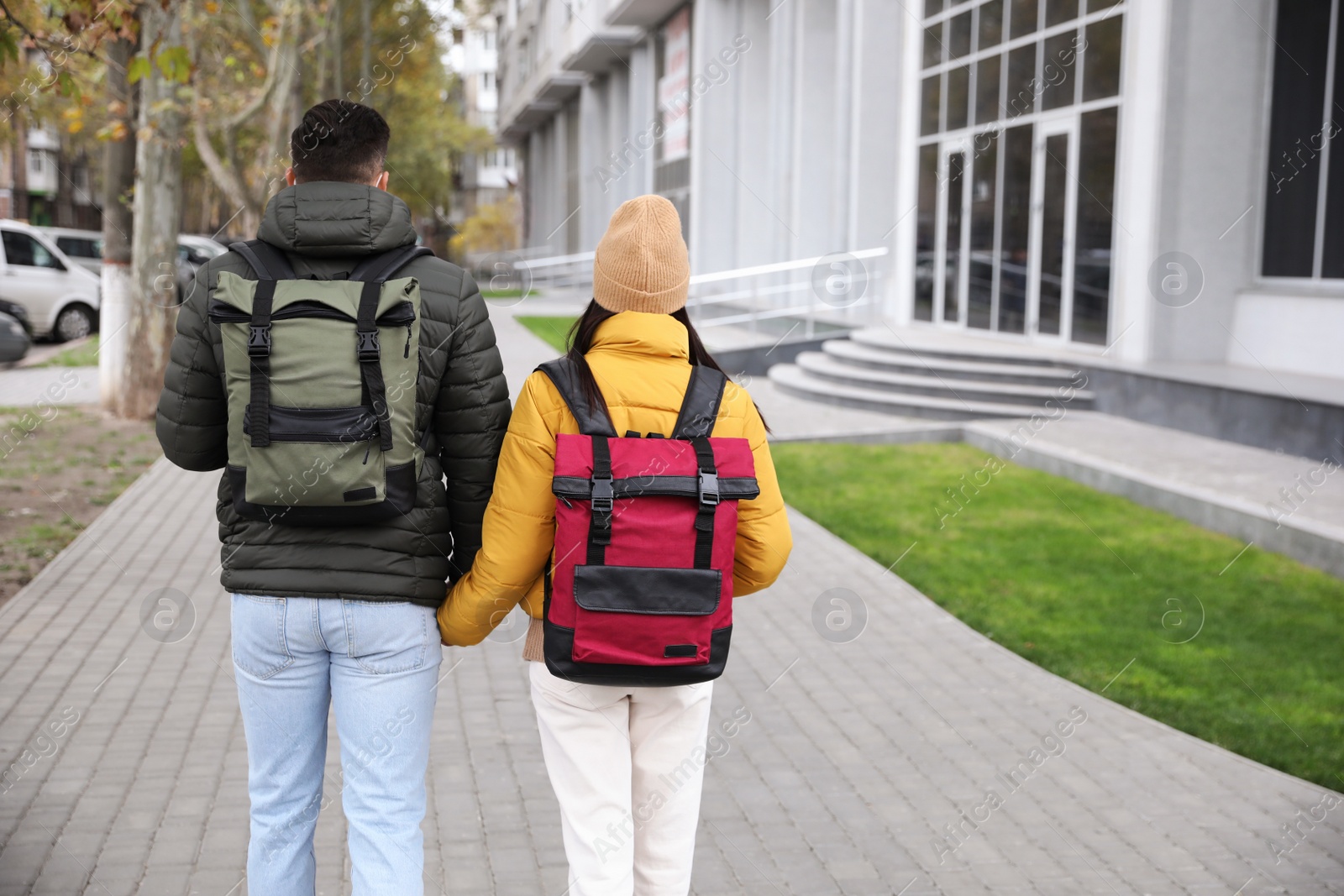 Photo of Couple with travel backpacks on city street, back view. Urban trip