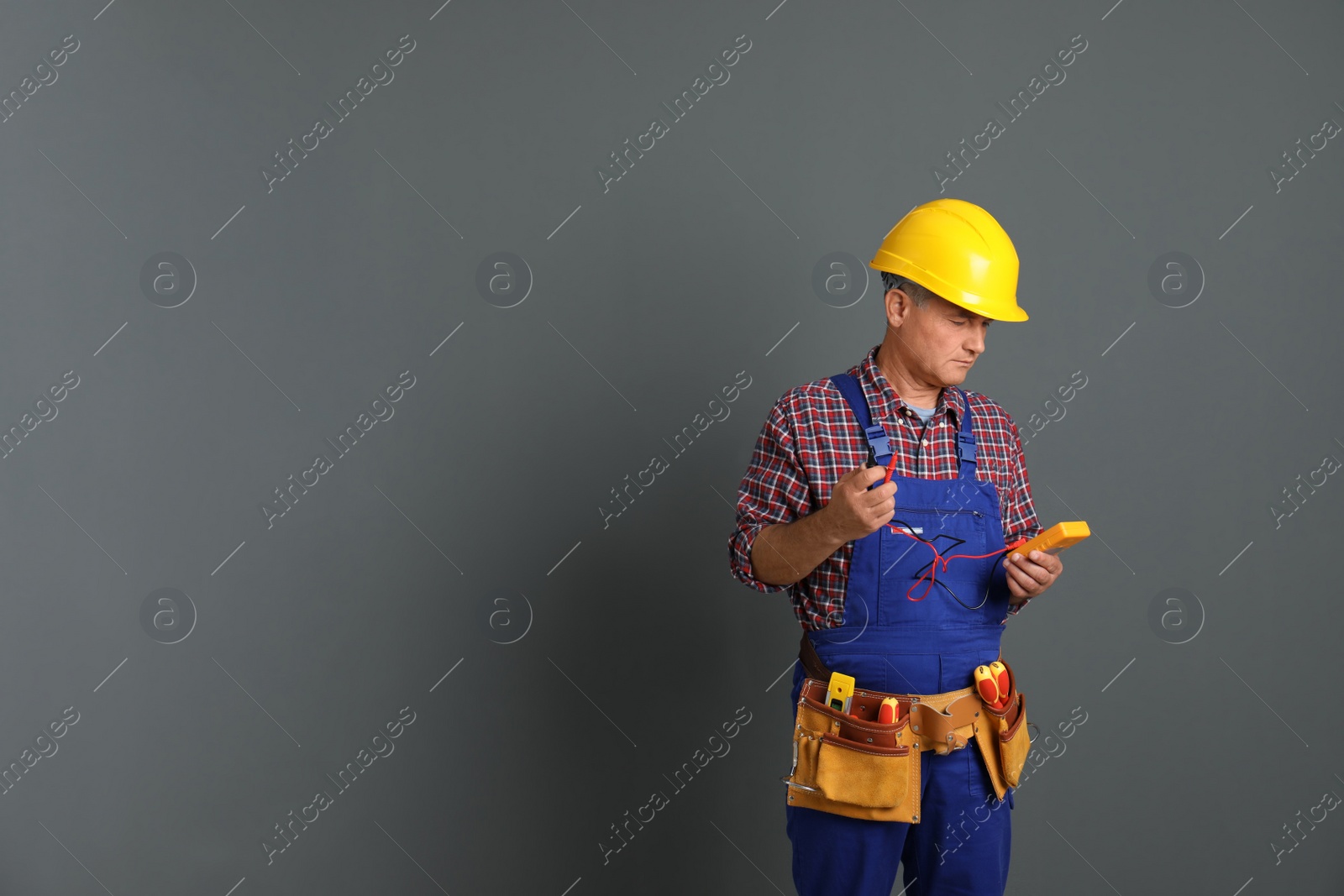 Photo of Electrician with multimeter wearing uniform on gray background. Space for text