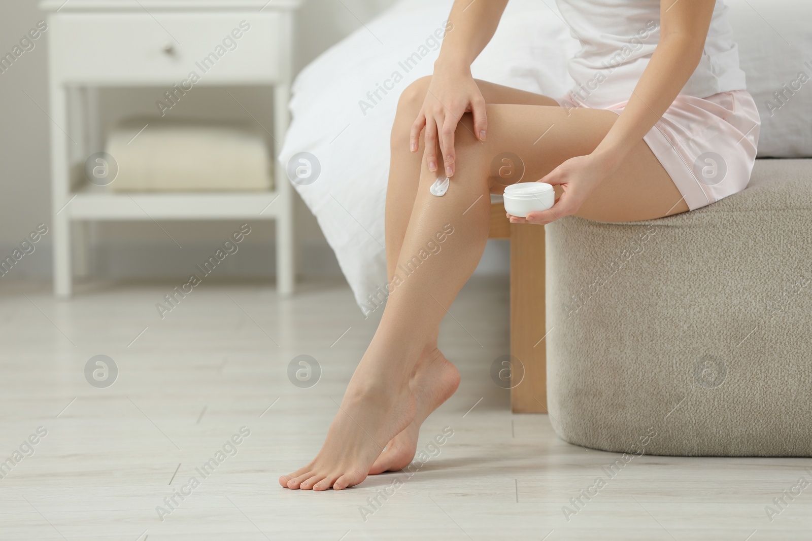 Photo of Young woman applying body cream on leg in bedroom, closeup. Space for text