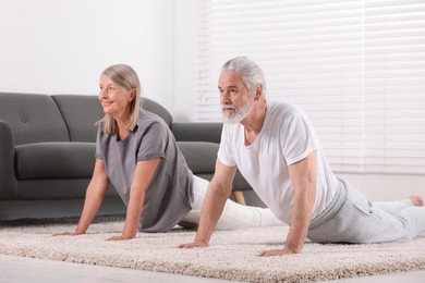 Photo of Senior couple practicing yoga on carpet at home. Healthy lifestyle