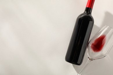 Bottle of expensive red wine and wineglass on light grey background, top view. Space for text
