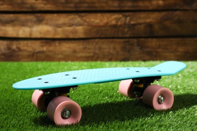 Light blue skateboard with pink wheels on green grass near wooden wall