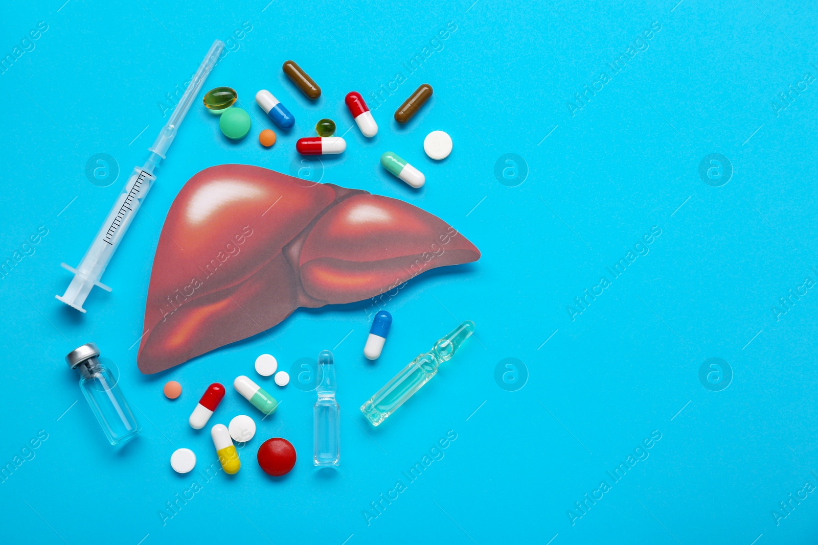 Photo of Paper liver, syringe, vials and pills on light blue background, flat lay with space for text. Hepatitis treatment