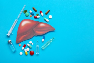 Paper liver, syringe, vials and pills on light blue background, flat lay with space for text. Hepatitis treatment